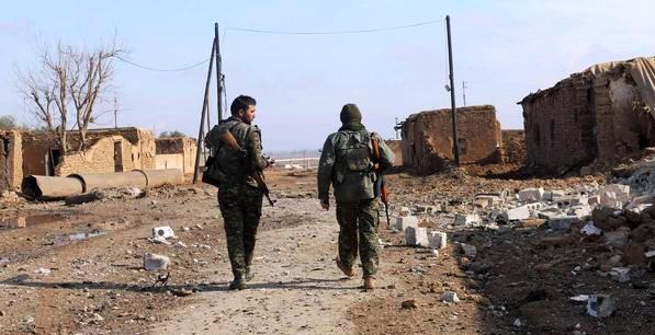 Members of the Kurdish People's Protection Units (YPG) walk past an area damaged by what activists said was a car blown up by a suicide bomber loyal to the Islamic State, in an attempt to target a YPG headquarter in Al-Hras village in Ras Al-Ain countryside November 23, 2014. REUTERS/Rodi Said (SYRIA - Tags: POLITICS CIVIL UNREST CONFLICT)