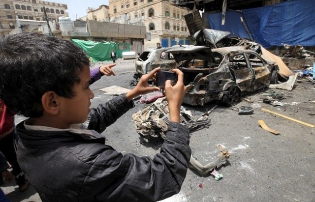 boy takes pictures for the wreckage of a car at the site of a car bomb attack in Yemen's capital Sanaa