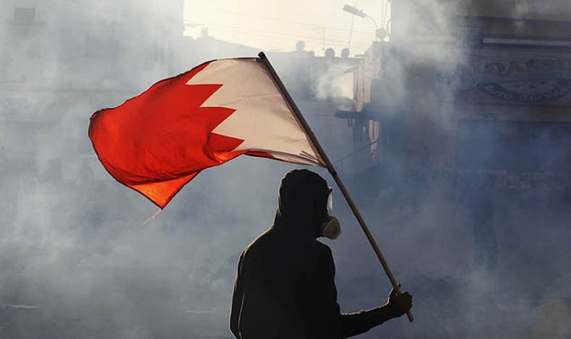 A protester carries a Bahraini flag as they clash with riot police in the village of Bilad Al Qadeem south of Manama